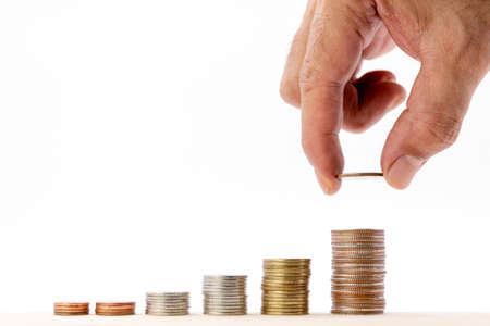 Closeup of human hand putting a coin on a pile of coins over white background, use for business and finance concepts.の写真素材