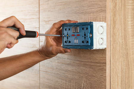 Electrician is using a screwdriver to install a power outlet in to a plastic box on a wooden wall.の写真素材