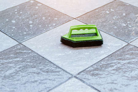 Close up a green plastic brush for scrubbing and cleaning floors placed on a wet tiled floor.の写真素材