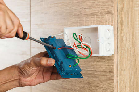 Hand of an electrician is using a screwdriver to attach the wires to the socket.の写真素材