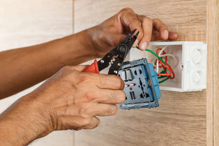 Electrician is stripping electrical wires in a plastic box on a wooden wall to install the electrical outlet.の写真素材