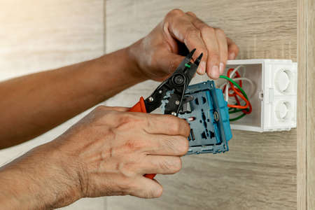 Electrician is stripping electrical wires in a plastic box on a wooden wall to install the electrical outlet.の写真素材