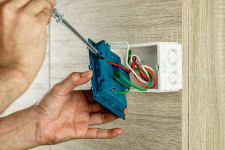 Remove the power electric plug socket from the outlet box on the wooden wall to check the voltage with a screwdriver.の写真素材