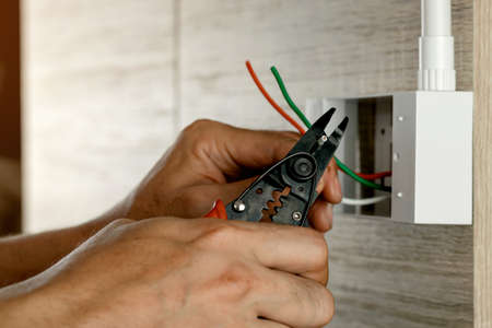 Electrician is stripping electrical wires in a plastic box on a wooden wall to install the electrical outlet.の写真素材