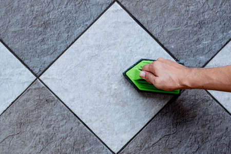 Top view of a human hand are using a green color plastic floor scrubber to scrub the tile floor with a floor cleaner.の写真素材