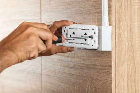 Electrician is using a screwdriver to install the electric power socket in to a plastic outlet box on a wooden wall.の写真素材