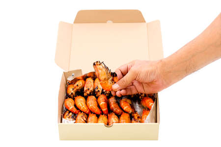 Close up a human hand pick up a grilled river prawn in a paper box isolated on white background.の写真素材