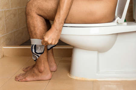 Close-up of a man's legs sitting stool on the toilet bowl.の写真素材