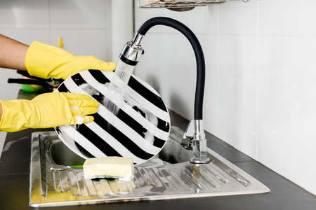 Close up human hands in yellow rubber gloves washing dishes in the kitchen sink.の写真素材