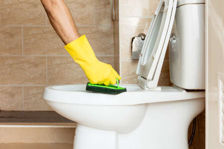 Human hand in a yellow rubber glove is using a plastic brush to scrub the toilet bowl.の写真素材