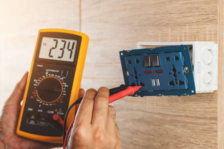 Using a digital meter to measure the voltage at an electric outlet socket box isolated on white background.の写真素材