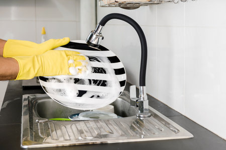 Human hands in yellow rubber gloves washing dishes in the kitchen sink.の写真素材