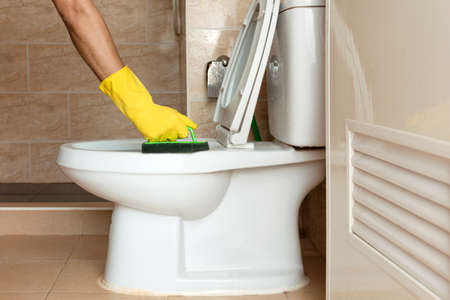 Human hand in a yellow rubber glove is using a plastic brush to scrub the toilet bowl.の写真素材