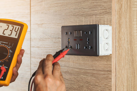 Electrician using a digital meter to measure the voltage at a wall socket on a wooden wall.の写真素材