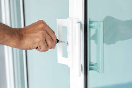 Close-up of man's hand opening a glass door with a key.の写真素材