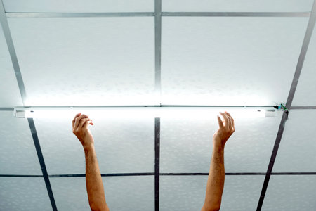 Close-up of a man's hand installing a long LED light bulb on the ceiling.の写真素材