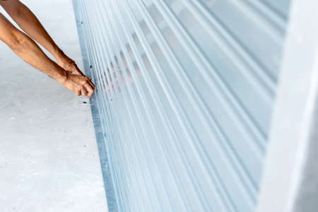 Close-up of man's hand using a key to open a rolling iron door.の写真素材
