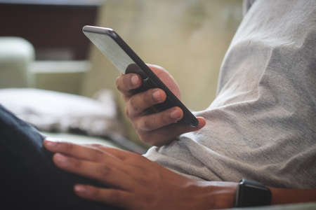 Man hold with smart phone at sit on sofa and use phone happily at home.の写真素材