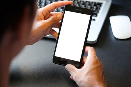 Cropped shot of young man using smart phone with white screen while sitting in modern office.