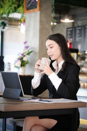 Businesswoman in formal suit wearing wireless earphone and working with tablet computer at modern cafe.の写真素材