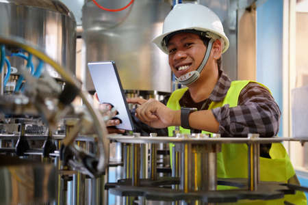 A technician in helmet using tablet while maintenance and check the operation of machines working in...