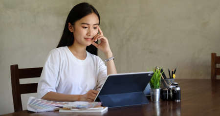 Portrait of young female designer is sitting at graphic studio in front of laptop computer while...