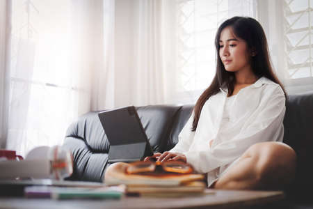 Smiling young woman in pajamas using digital tablet on couch.