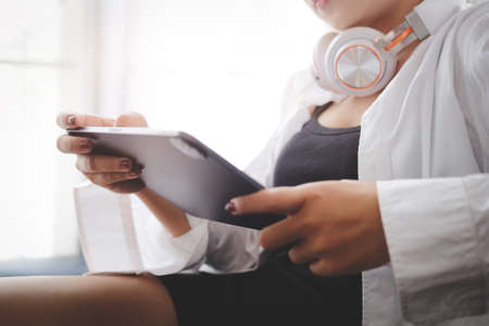 Smiling young woman in pajamas using digital tablet on couch.の写真素材