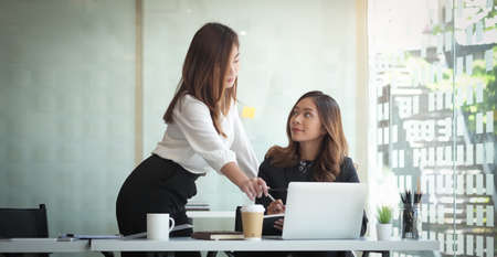 Business woman reading information on paperwork and using laptop working on desk.