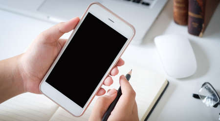 Mock up smartphone of hand holding black mobile phone with blank white screen.