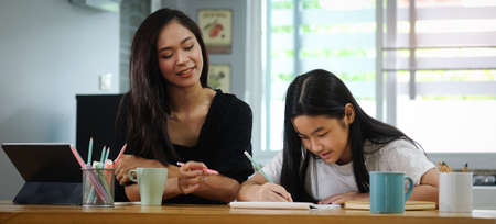 Asian mother helping her daughter doing homework with digital tablet at home.の写真素材
