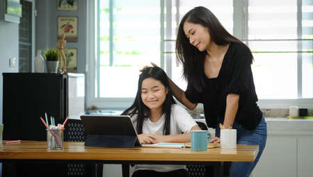 Asian mother helping her daughter doing homework with digital tablet at home.の写真素材