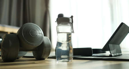 Water bottles, dumbbells and laptop on wooden floor. Workout training at home.の写真素材