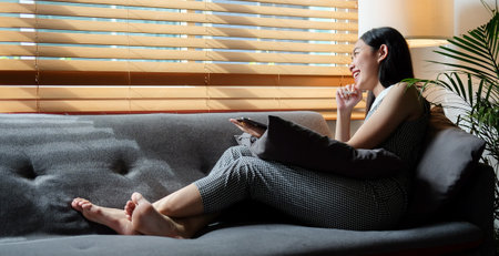 Smiling young woman sitting on comfortable sofa and using digital tablet.