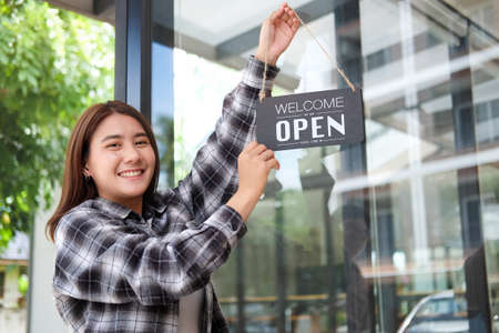 Happy waitress woman turning open sign board on glass door coffee shop.