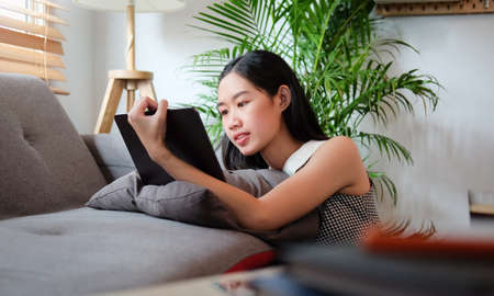 Asian girl using digital tablet while sitting in living room.