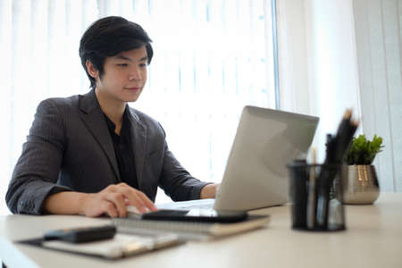 Confident businessman sitting in modern office and working with laptop computer.の写真素材