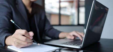 Cropped shot businessman making note on notebook and working with laptop.