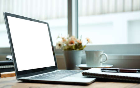 Mock up laptop computer, coffee cup and notebook on wooden table near window.の写真素材