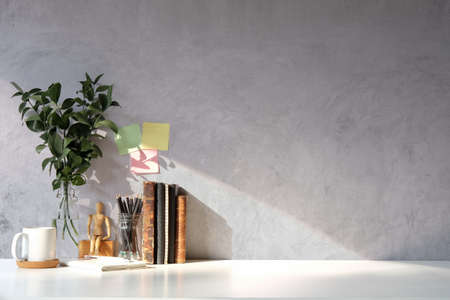 Books, coffee cup, notebook and potted plant on white table with concrete wall. Copy space.
