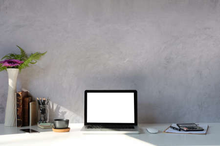 Front view laptop computer, calculator, books and coffee cup on white table with concrete wall.