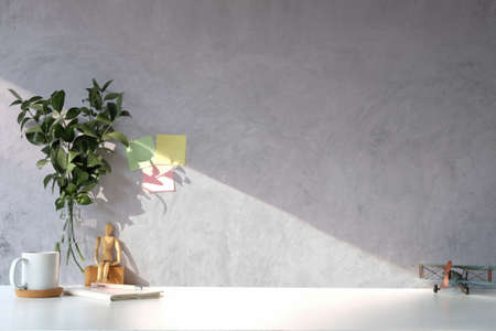 Coffee cup, plant and notebook on white table with concrete wall.の写真素材