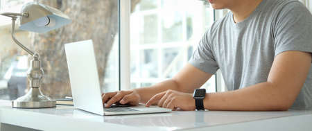 Cropped shot young man working with computer laptop in cafe.