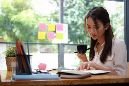 Businesswoman drinking coffee and checking information at her office desk.の写真素材