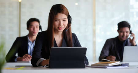Asian woman agent operator telemarketer wearing wireless headset working in customer care support service team office.の写真素材