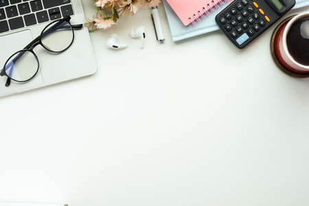 Laptop computer, coffee cup, glasses, calculator and notebook on white office desk. Top view.