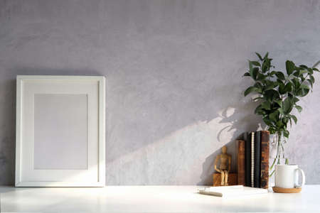 Photo frame, houseplant, coffee cup and books on white table with cement wall.の写真素材