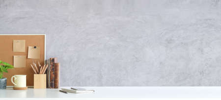 Wooden board with sticky notes, coffee cup and books on white table with cement wall. Copy space for products display montage.の写真素材