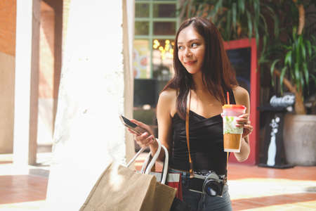Young Asian woman holding shopping bags and smart phone standing on the city street.の写真素材