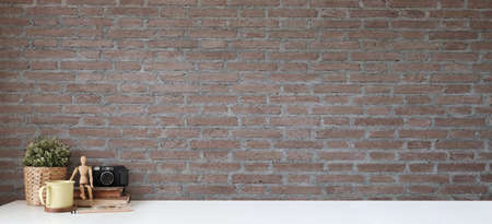 Stylish workspace with houseplant, camera and coffee cup on white table with brick wall.の写真素材